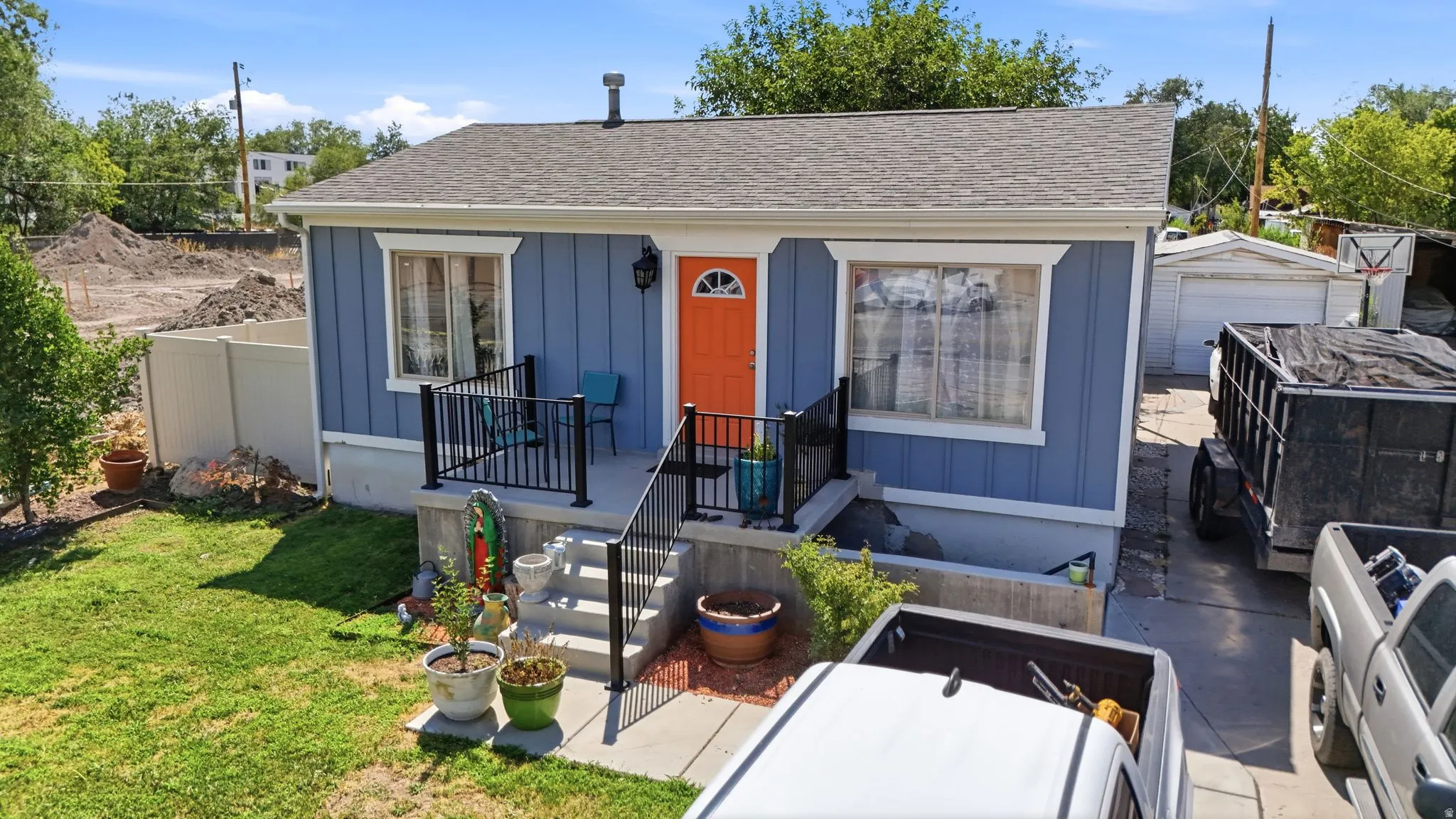 Charming exterior with blue vertical siding, a bright orange entry door, and a gray shingle roof