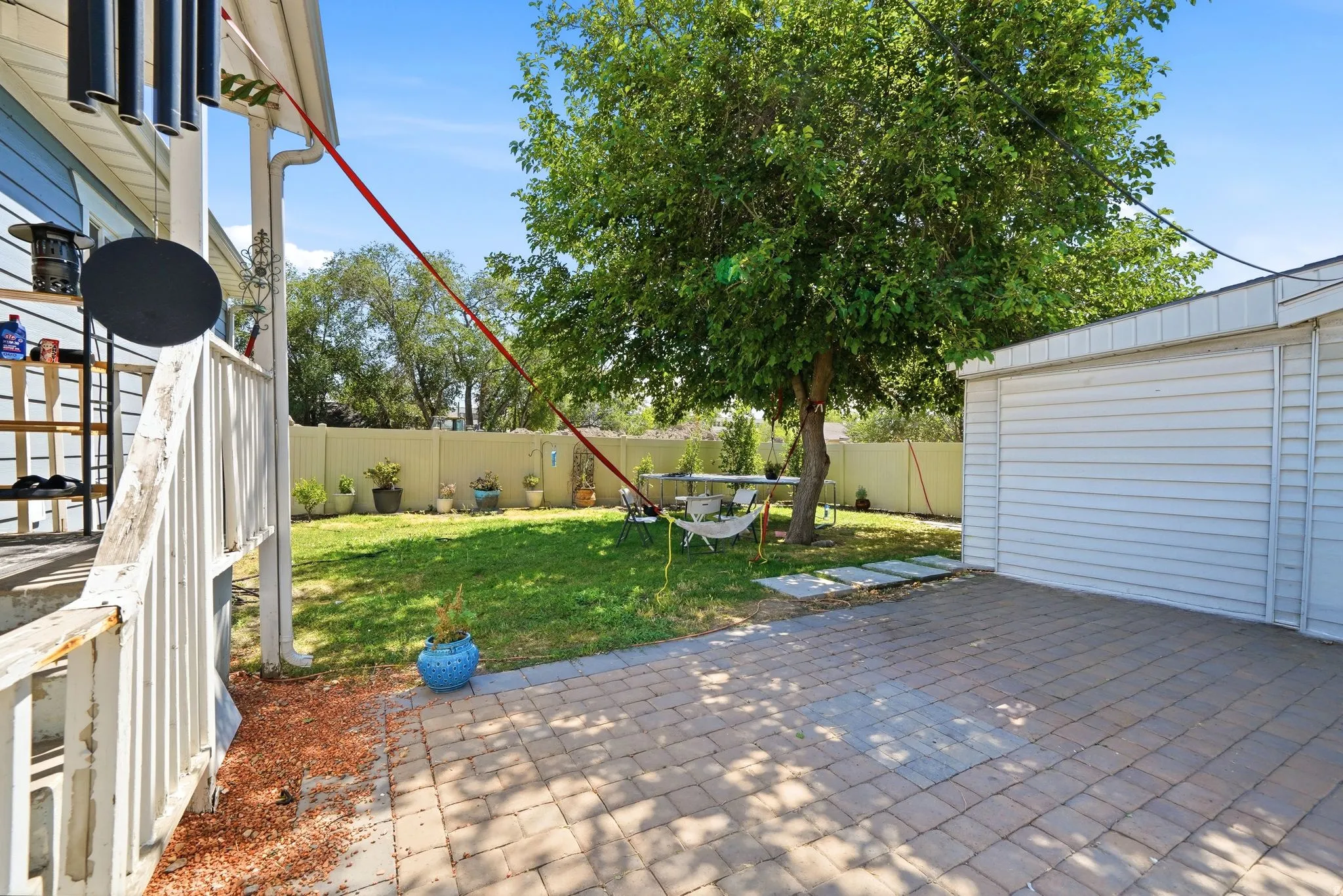 Expansive backyard featuring a paver patio, a detached garage with horizontal siding, a substantial shade tree, and a grassy area with perimeter fencing