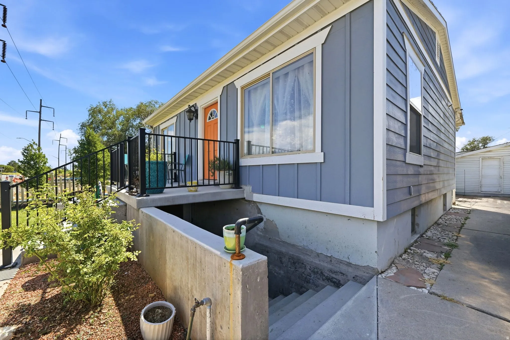 Exterior featuring basement walkout, blue siding, white trim, a vibrant orange entry door, and a black metal railing