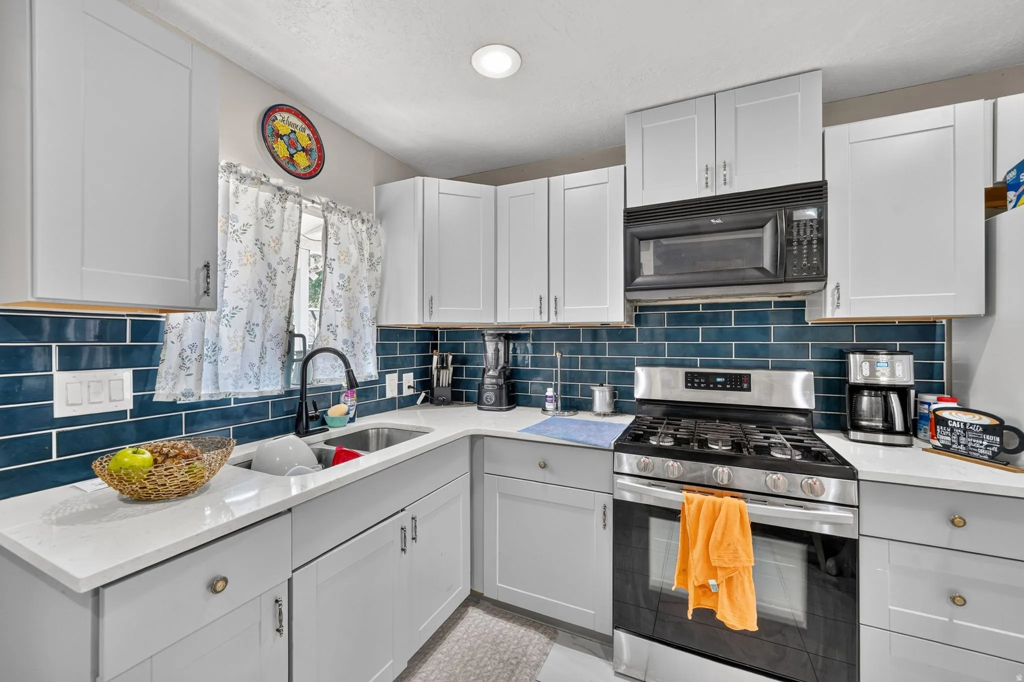 Contemporary kitchen featuring light gray shaker cabinetry, white countertops, a deep blue subway tile backsplash, a stainless steel gas range, and a built-in microwave
