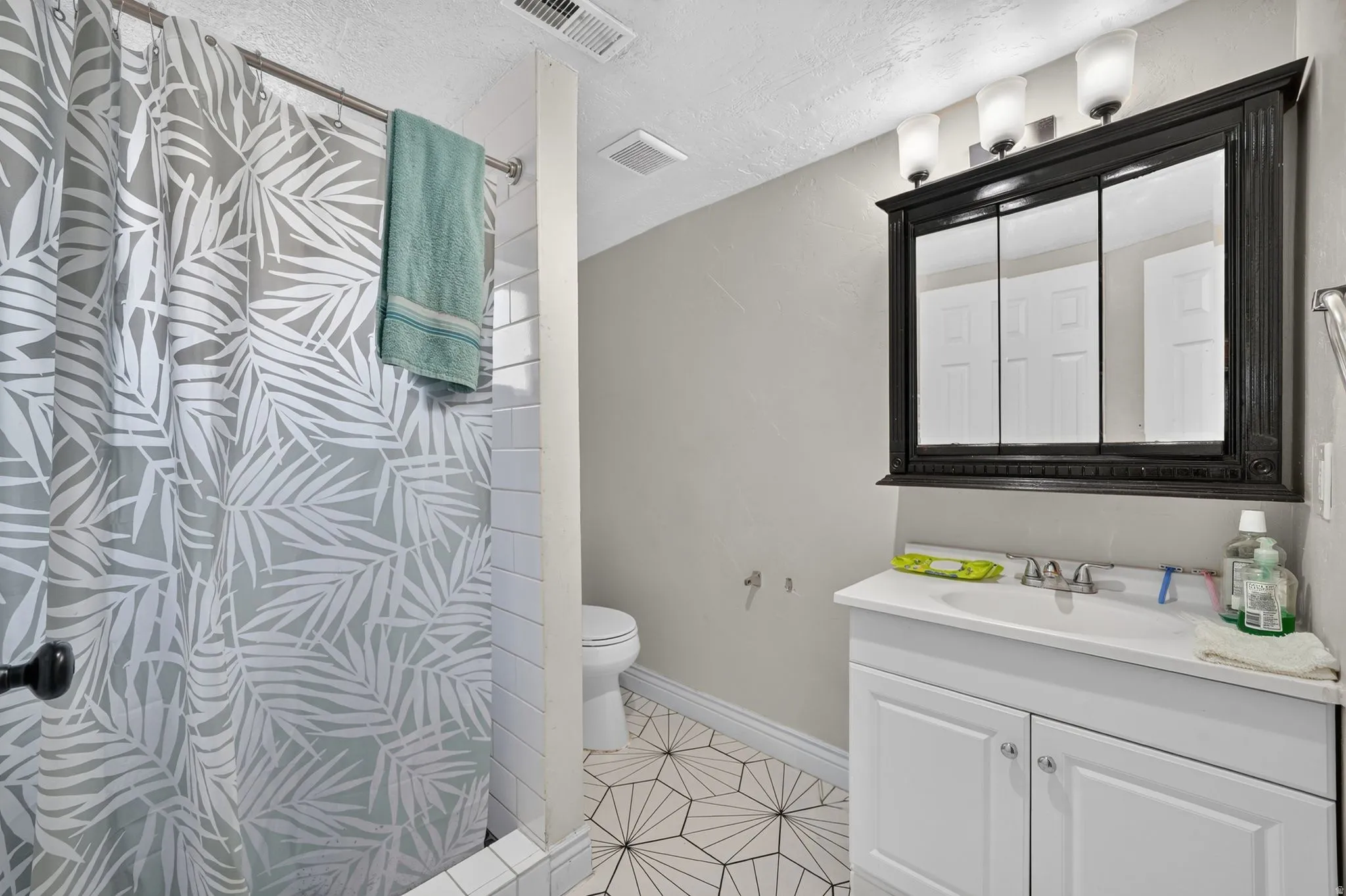 Bathroom featuring a white vanity with silver-tone fixtures, a dark wood-finish medicine cabinet with integrated lighting, and geometric patterned floor tiling