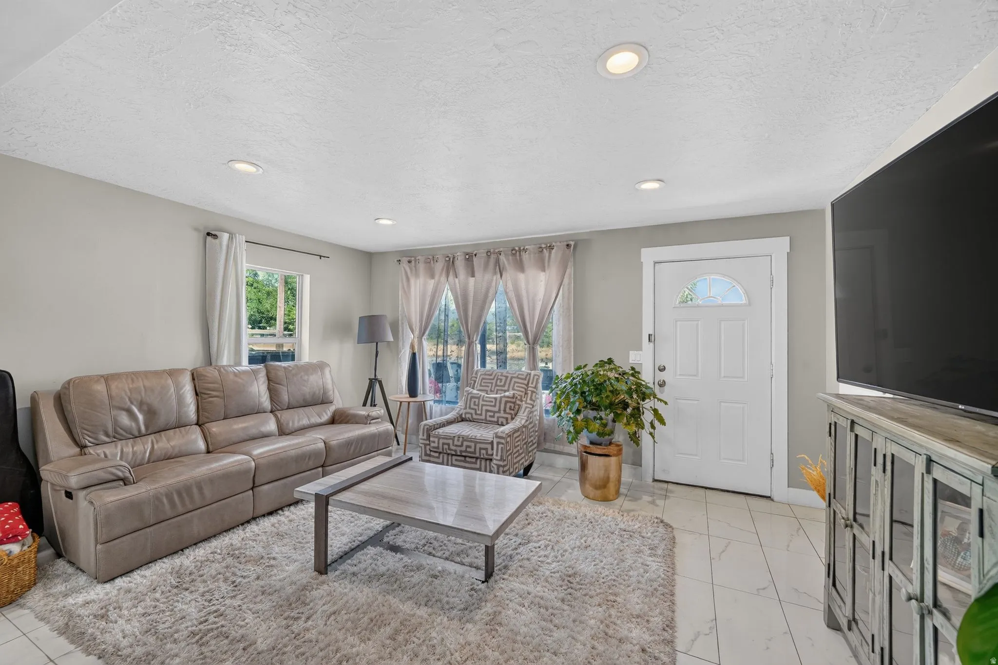 Spacious living area featuring light-toned walls, recessed ceiling lighting, and tile flooring
