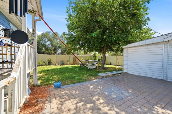 Expansive backyard featuring a paver patio, a detached garage with horizontal siding, a substantial shade tree, and a grassy area with perimeter fencing