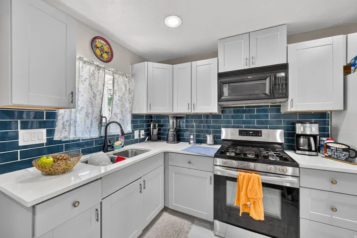Contemporary kitchen featuring light gray shaker cabinetry, white countertops, a deep blue subway tile backsplash, a stainless steel gas range, and a built-in microwave