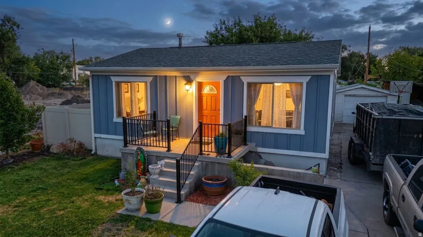 Exterior featuring blue vertical siding, a covered porch with black railings, a contrasting orange entry door, and a dark shingled roof