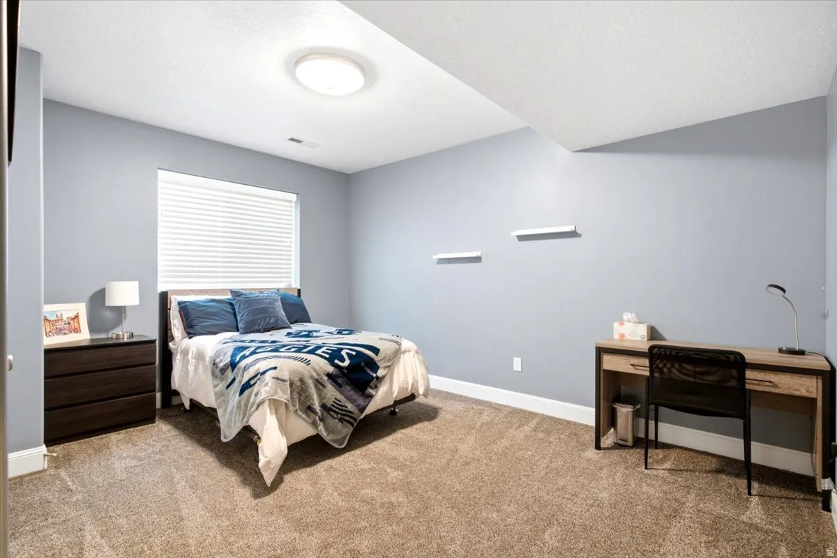 Bedroom featuring light blue walls, a rectangular window with blinds, and neutral-toned carpeting