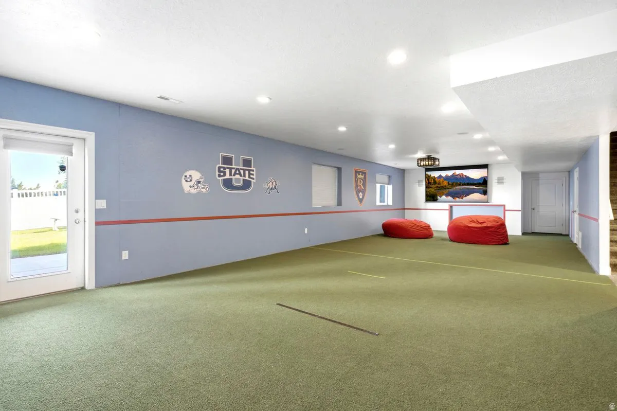 Recessed lighting illuminating the expansive green flooring, integrated projector screen, and a large white French patio door