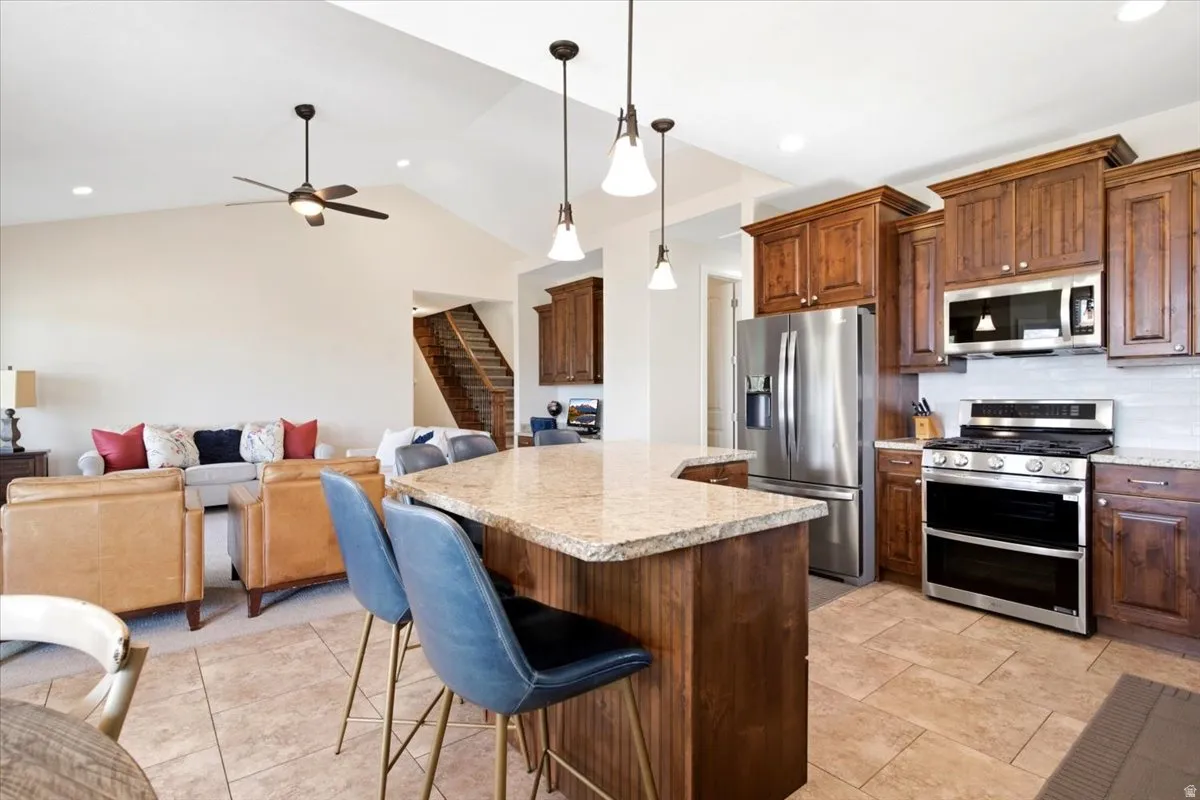 Open-concept kitchen featuring granite countertops, stainless steel appliances, wood cabinetry, and pendant lighting