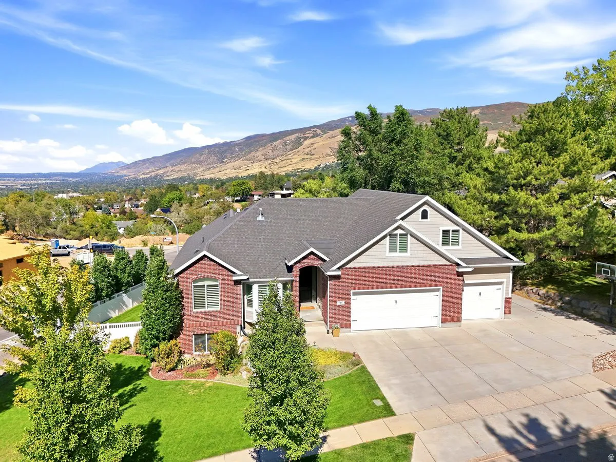 Brick and siding exterior, multi-car garage, concrete driveway, front lawn with landscaping, and a mountain backdrop
