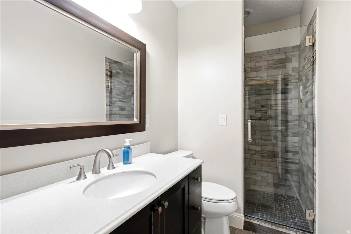 Bathroom featuring a dark wood-finish vanity with a white countertop and undermount sink, a framed mirror, and a glass-enclosed shower with stacked stone-look wall tile