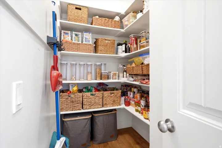 Extra-large walk-in pantry featuring white shelving, wood-finish flooring, and ample storage space