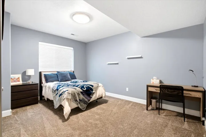 Bedroom featuring light blue walls, a rectangular window with blinds, and neutral-toned carpeting