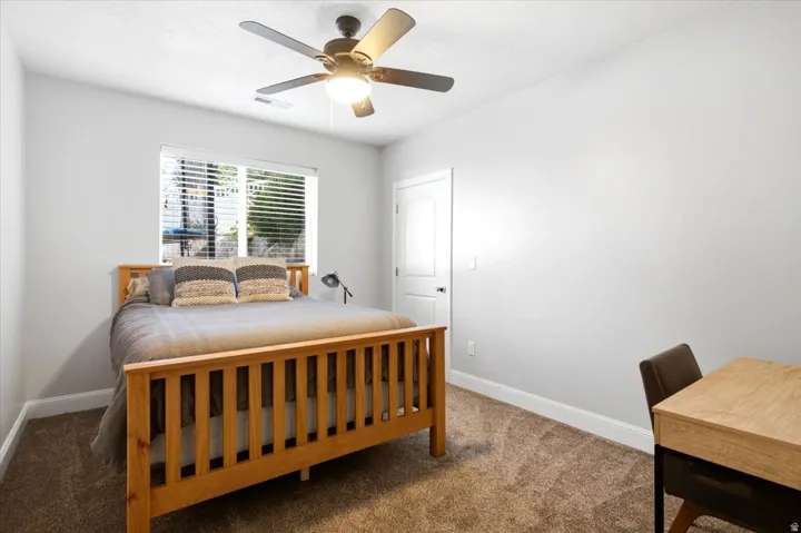 Bedroom featuring light gray walls, brown carpet, a window with horizontal blinds, a white door, and a ceiling fan with integrated lighting