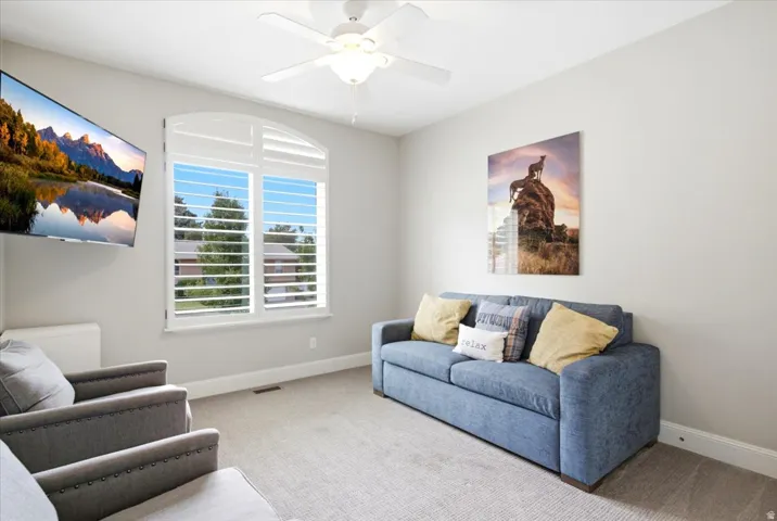 Carpeted room featuring a ceiling fan with integrated lighting, a wall-mounted television, and a window with custom arched plantation shutters