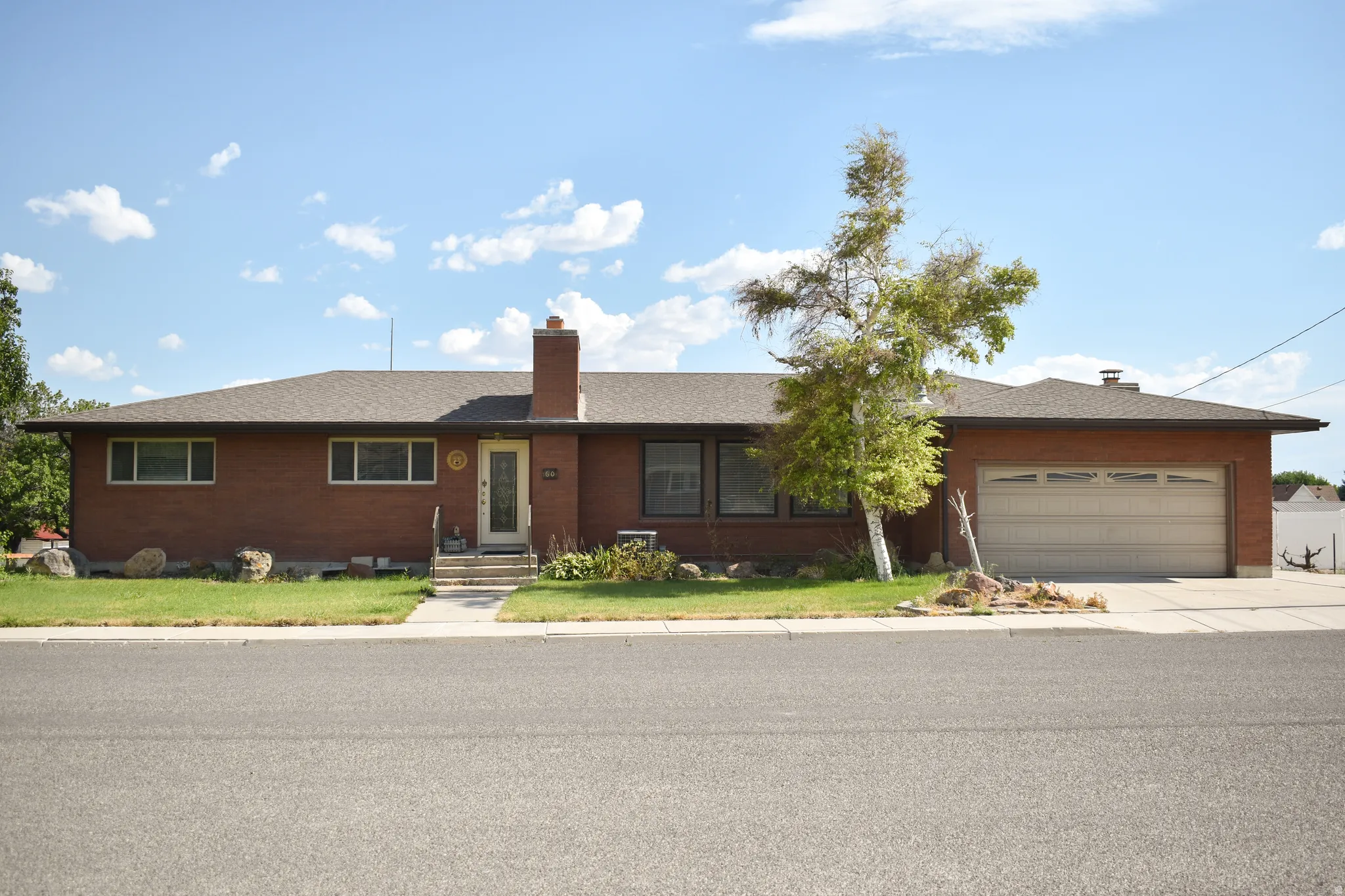 Brick exterior residence featuring a two-car garage, front walkway, and mature landscaping