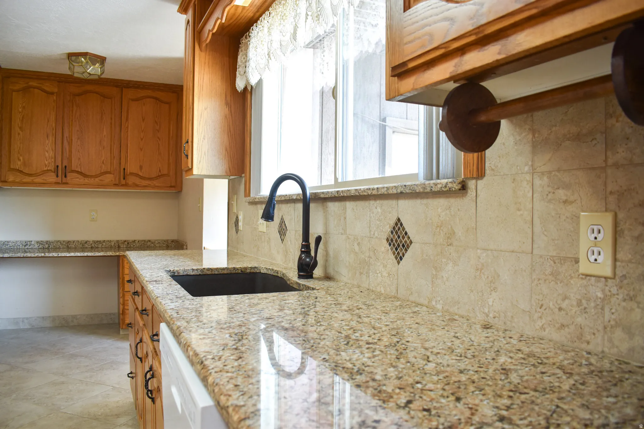 Kitchen featuring granite countertops, wood cabinetry, a black single-basin sink, and a tiled backsplash with decorative accents