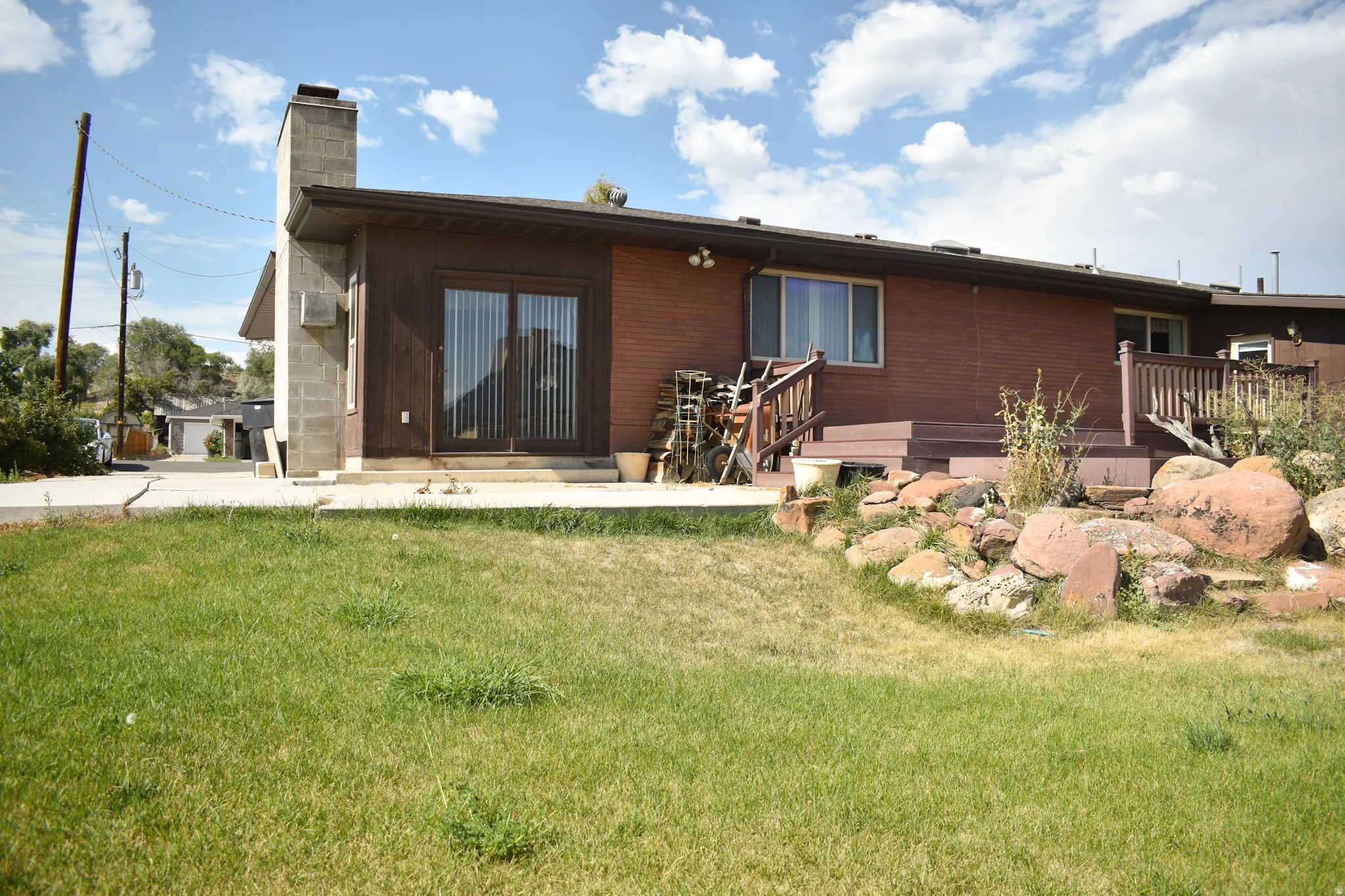 Rear exterior featuring a sliding glass door, brown brick siding, a wood deck with railings, and a concrete block chimney
