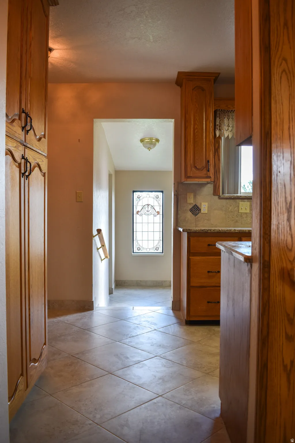 Hallway featuring tile flooring, wood cabinetry with black hardware, and a decorative window