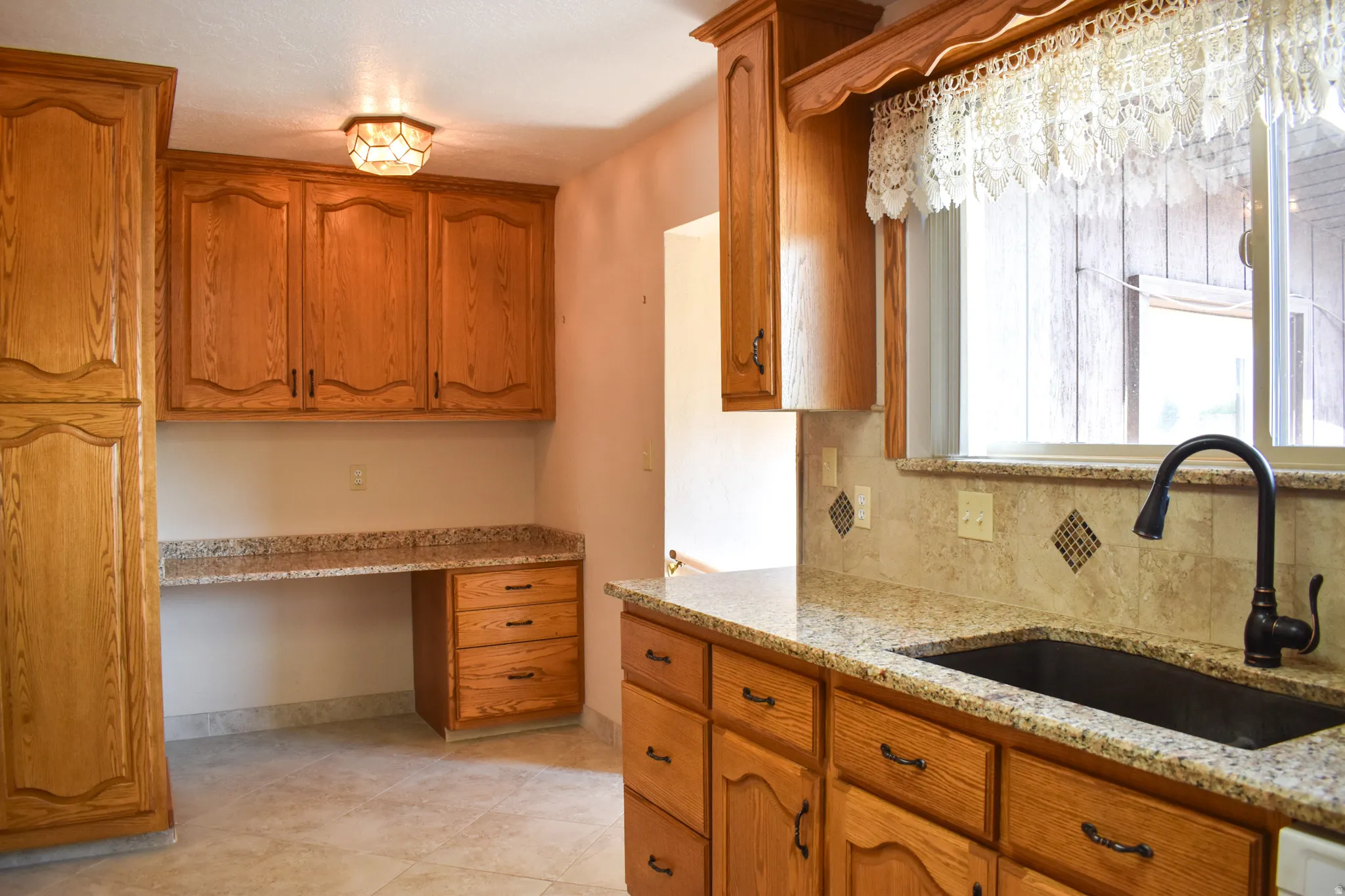 Kitchen area featuring extensive cabinetry with wood-finish doors, granite countertops, and a built-in desk space