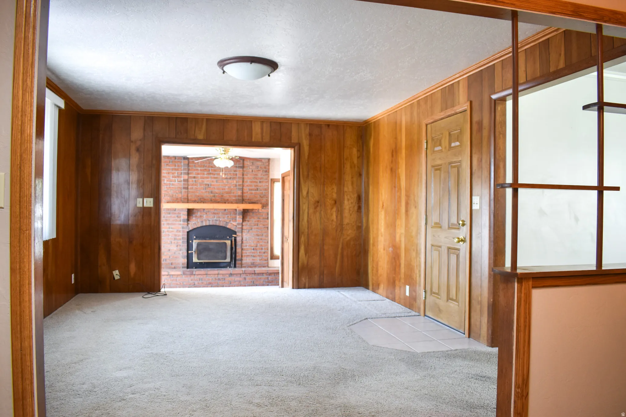 Wood paneling throughout this interior space, featuring a brick fireplace with a wood mantle and dark-toned firebox insert