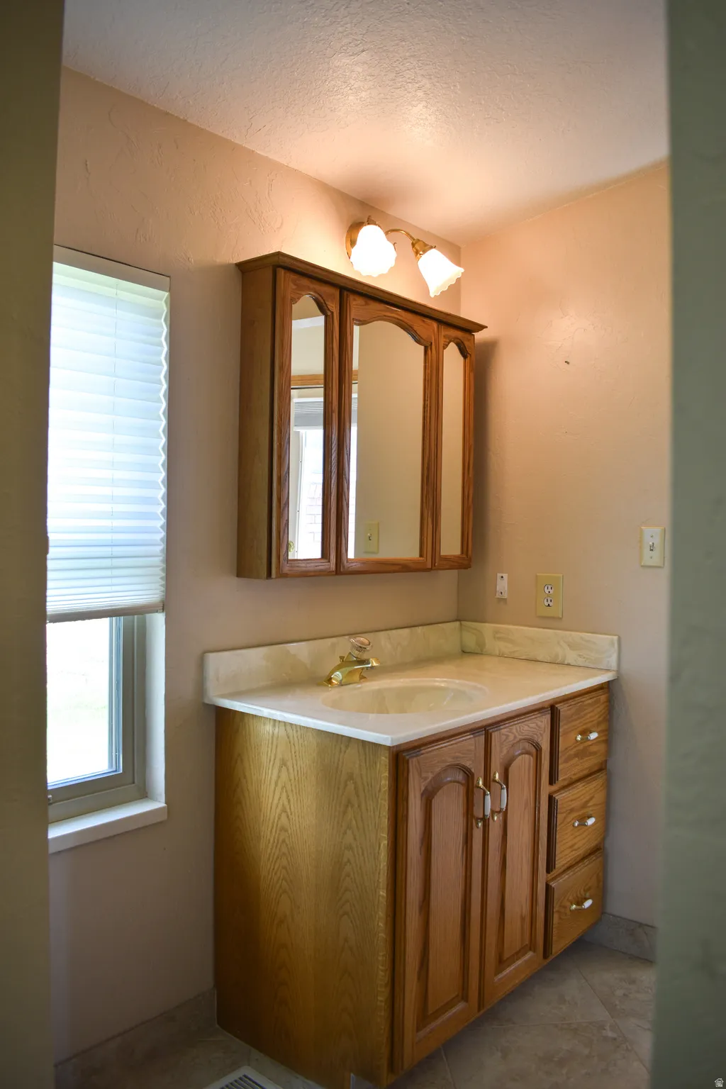Vanity featuring a light-colored countertop with an integrated sink, wood-finish cabinetry, and an overhead mirrored medicine cabinet