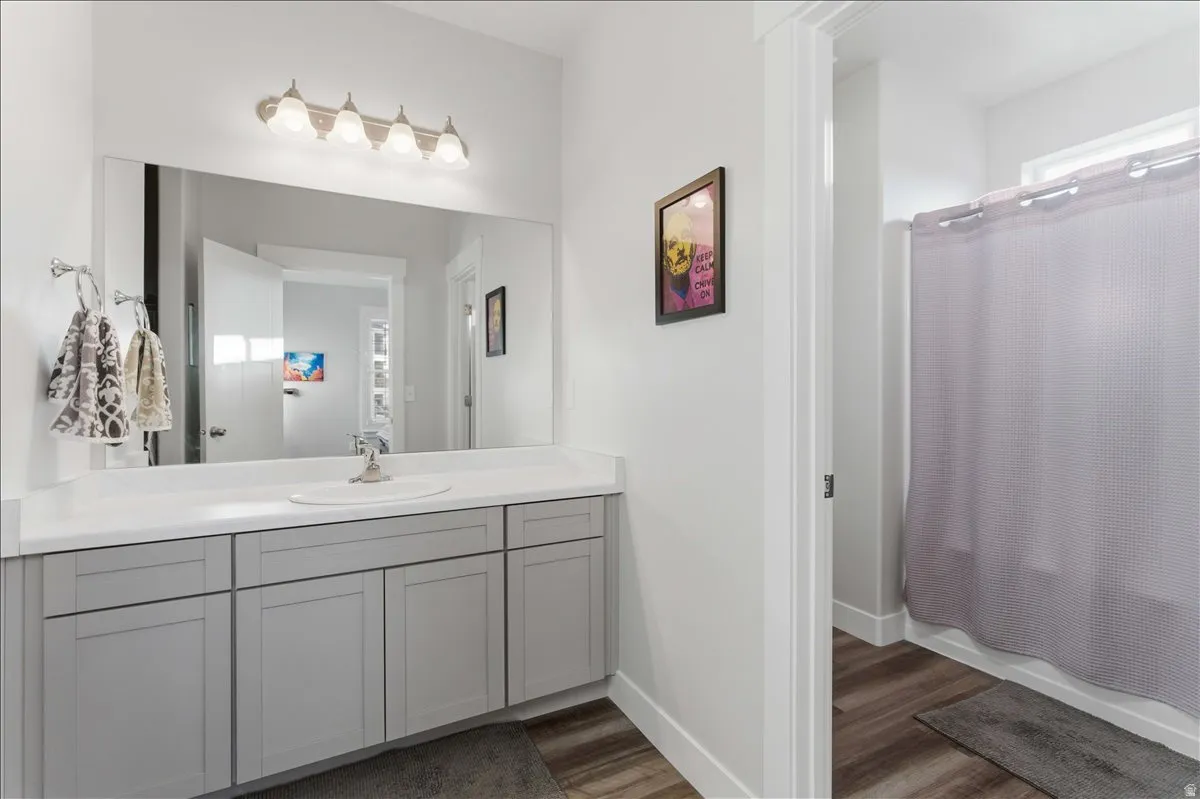 Bathroom vanity featuring a single basin sink set into a white countertop, extensive grey cabinetry, and a large mirror with overhead four-bulb lighting