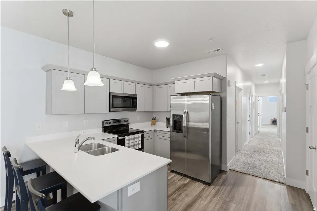Modern kitchen featuring light gray cabinetry, stainless steel appliances, a white countertop island with an undermount sink, and wood-finish flooring