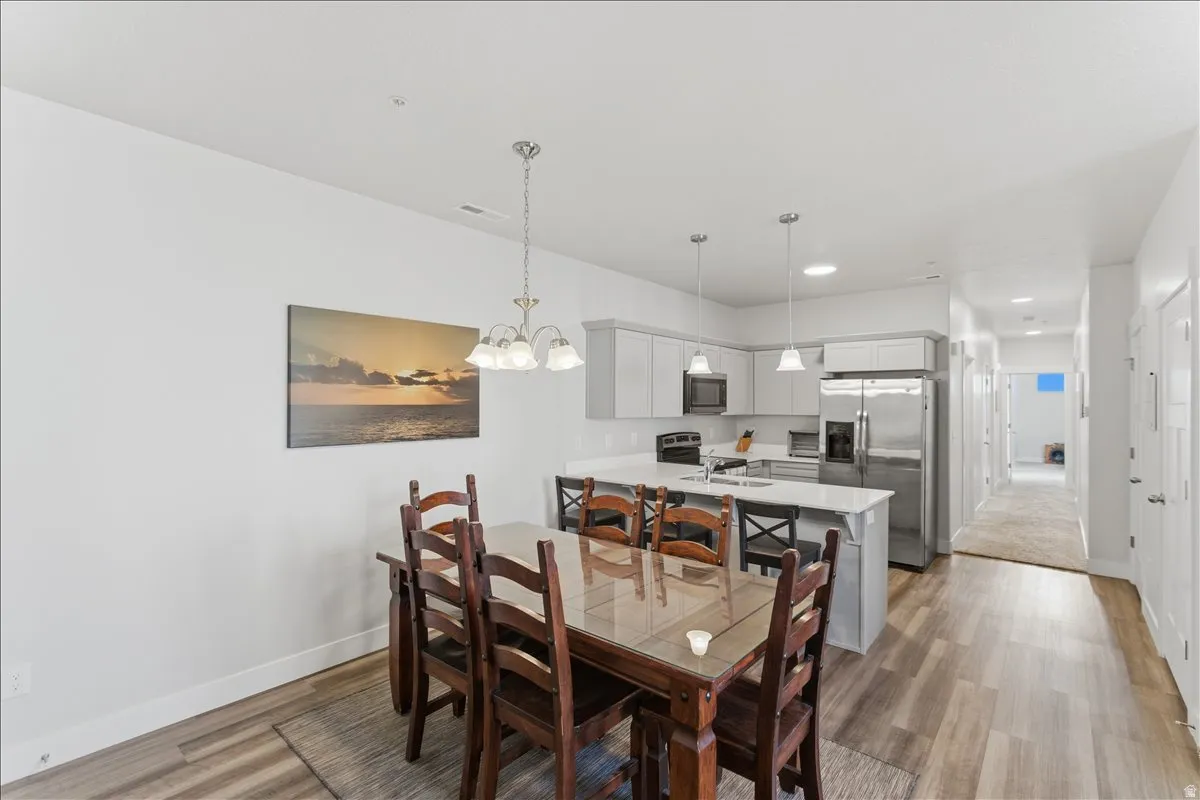Open-concept kitchen and dining area featuring wood-finish flooring, white walls, and a chandelier