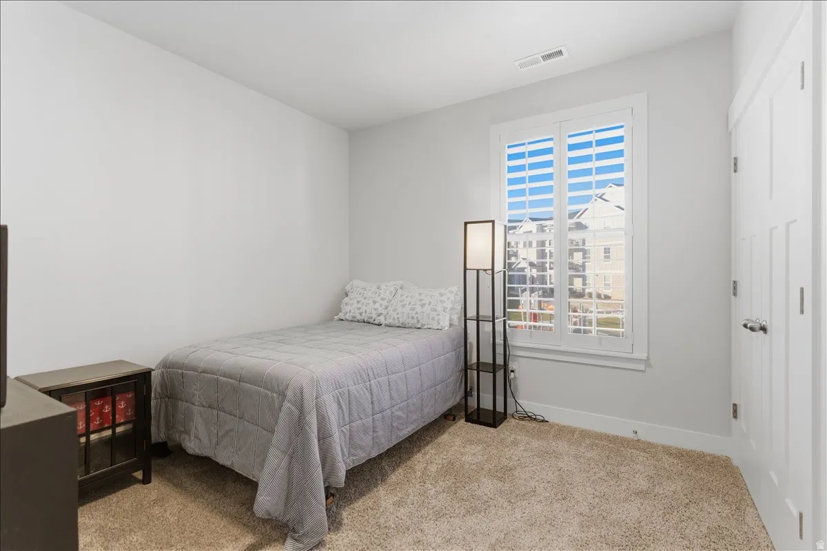 Carpeted room featuring a window with white plantation shutters and a white paneled door