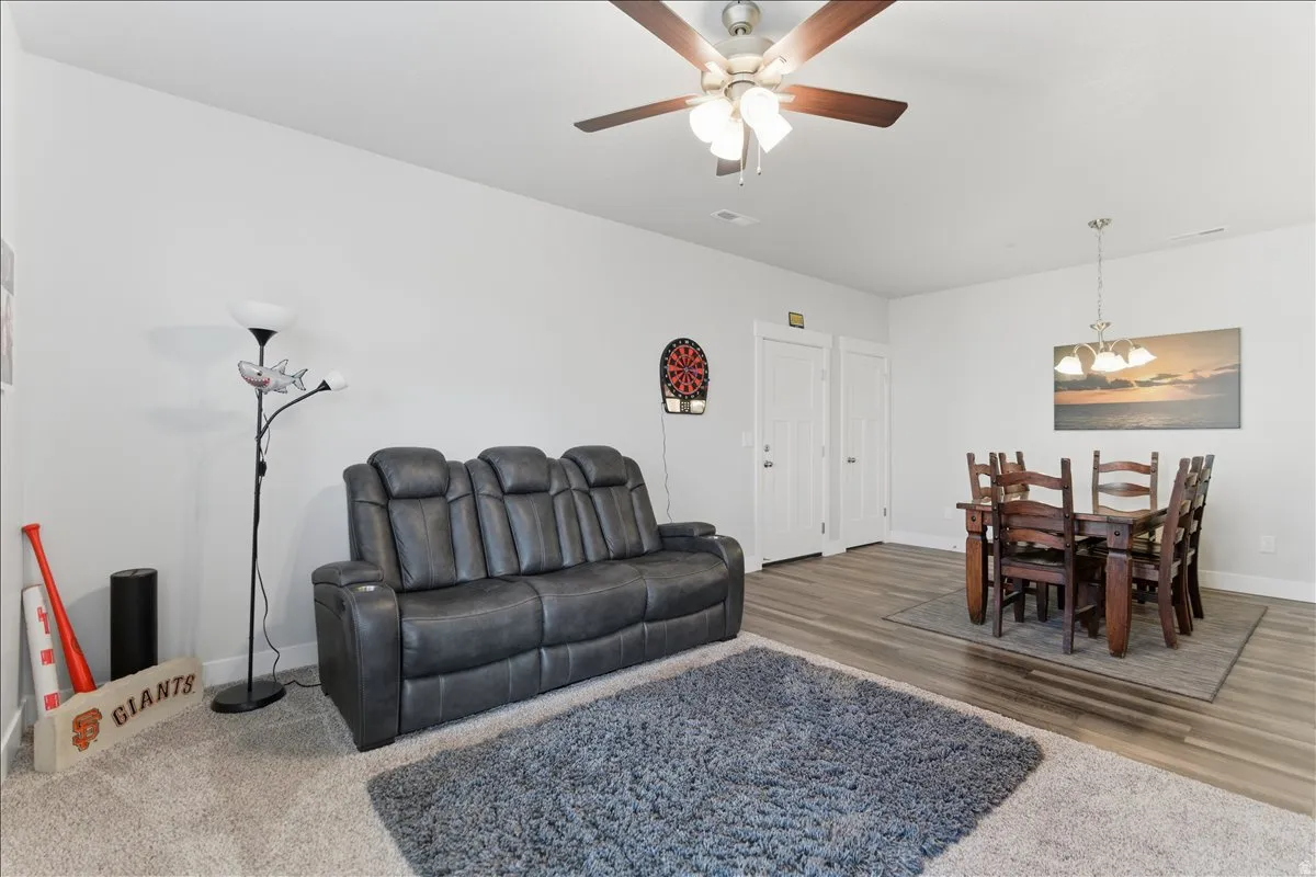 Open-concept living area featuring a ceiling fan with integrated lighting, two white panel doors, and wood-finish flooring extending into the dining space
