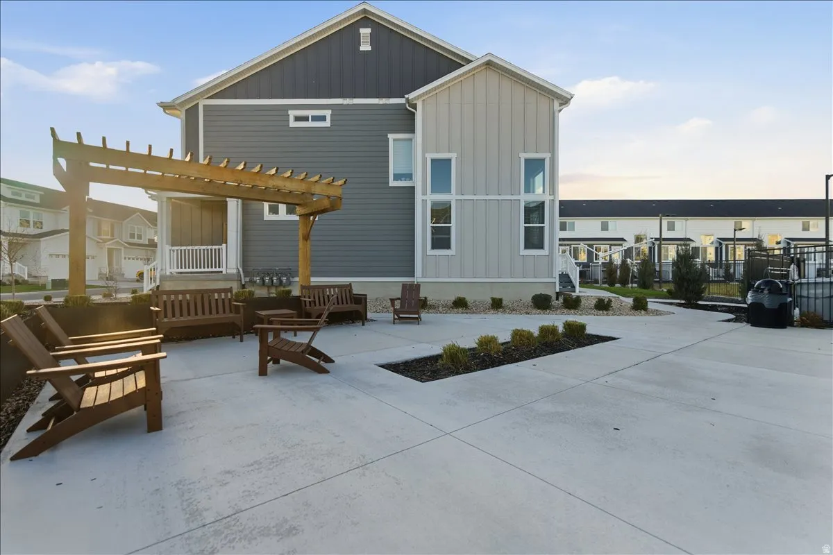 Expansive concrete patio area featuring a wooden pergola and landscaped beds