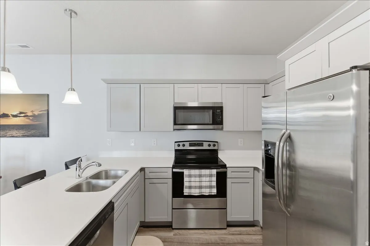 Modern kitchen featuring light gray shaker cabinetry, white countertops, and stainless steel appliances including a refrigerator, range, microwave, and dishwasher