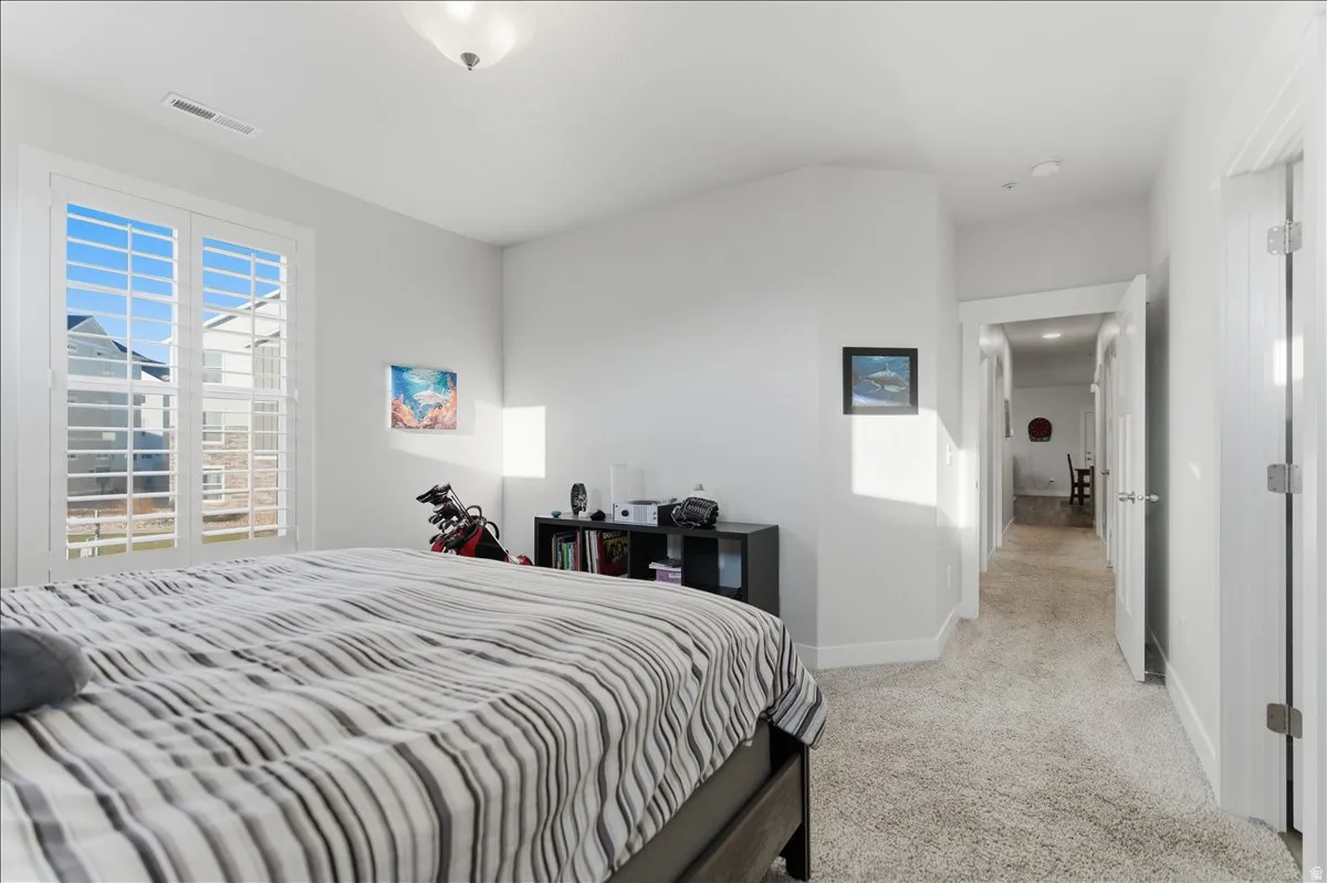 Spacious room featuring carpeting, a vaulted ceiling, and white plantation shutters on a large window