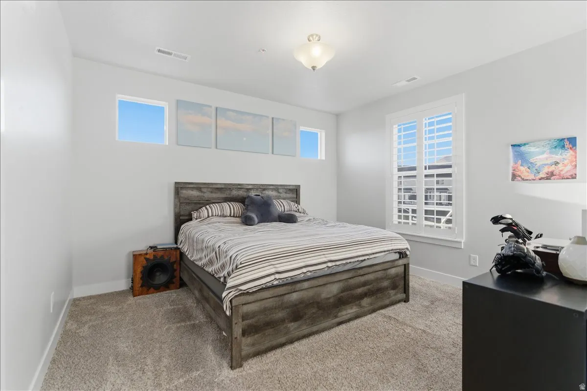 Spacious room with light gray walls, plush carpet, and white plantation shutters on a large window