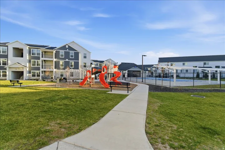 Expansive green space featuring a playground with red slides, a concrete pathway, a fenced swimming pool with a pergola, and multi-story residential buildings with balconies