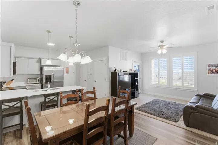 Open-concept living space featuring a dining area with a glass-top table, a kitchen with stainless steel appliances and light cabinetry, and a living area with large windows