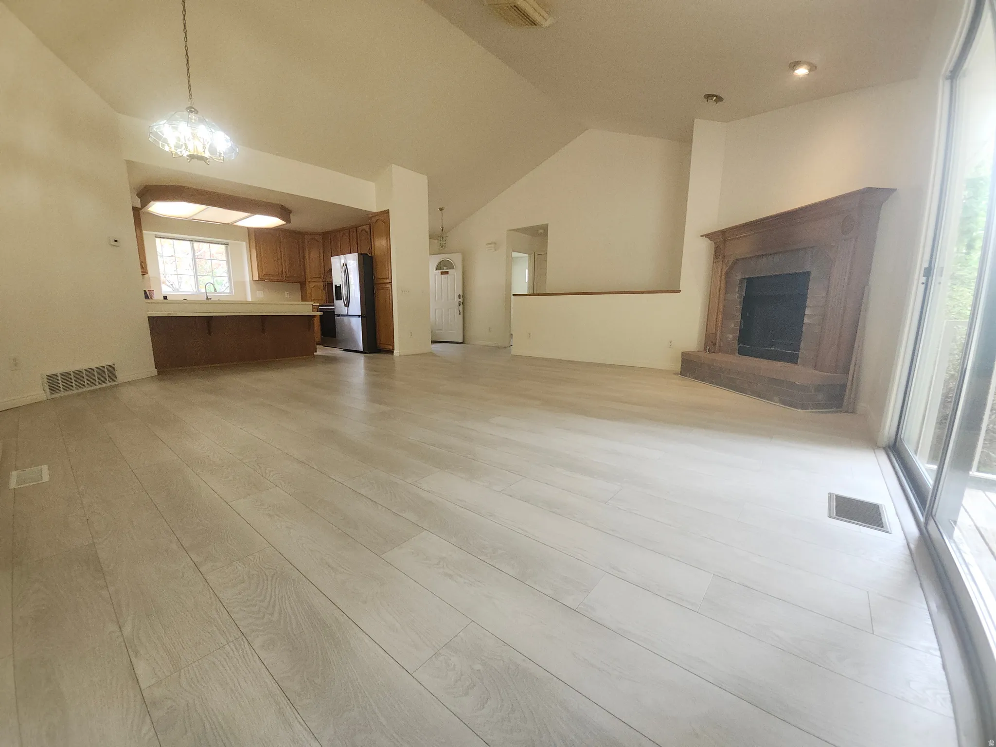 Wood-finish flooring throughout, vaulted ceilings, a fireplace with a wood mantel, and sliding glass doors