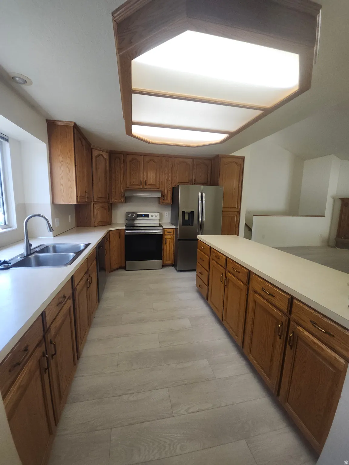 Kitchen with new stainless steel fridge,  featuring wood-finish cabinetry, light-toned countertops, and stainless steel appliances