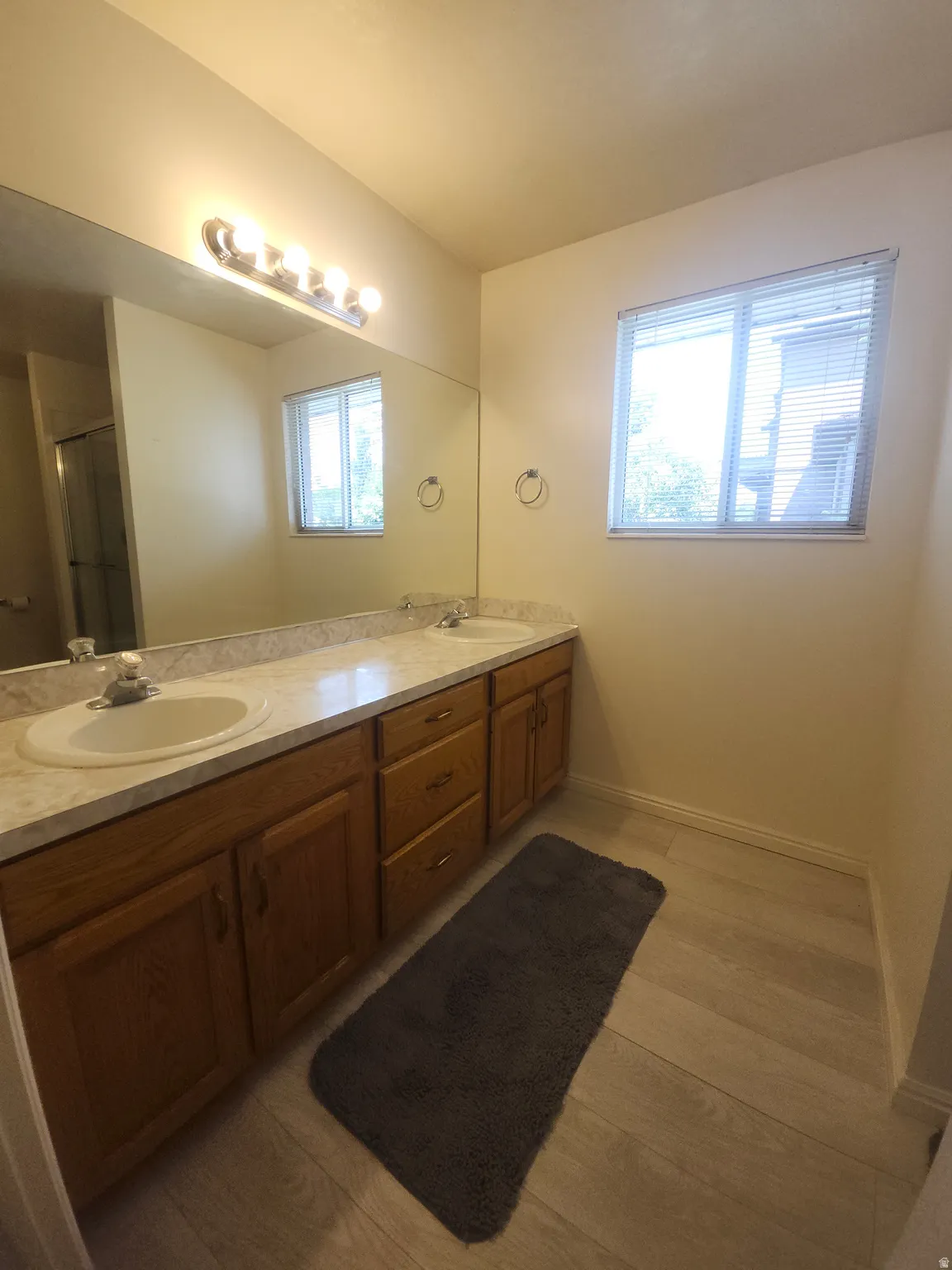 Primary Bathroom with Dual vanity with integrated sinks, wood-finish cabinetry, light-toned countertops, and wood-finish flooring