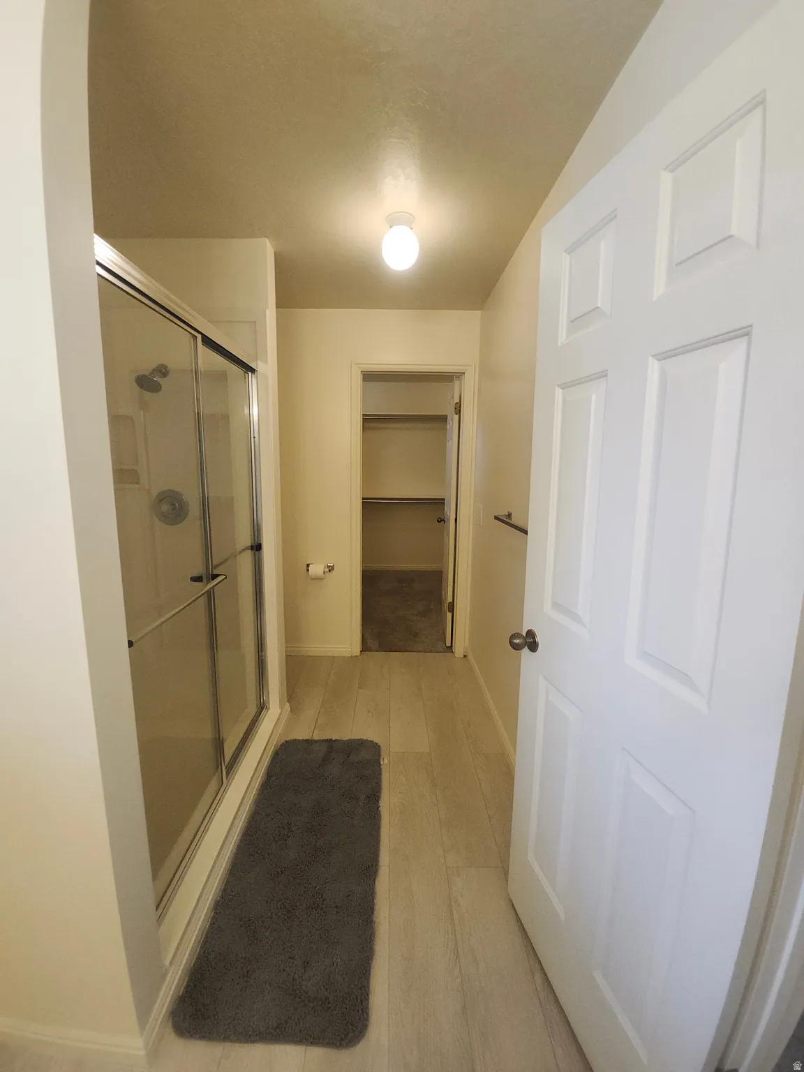 Primary Bedroom Shower, goes to walk-in shower with sliding glass enclosure, light wood-finish flooring, and a paneled interior door