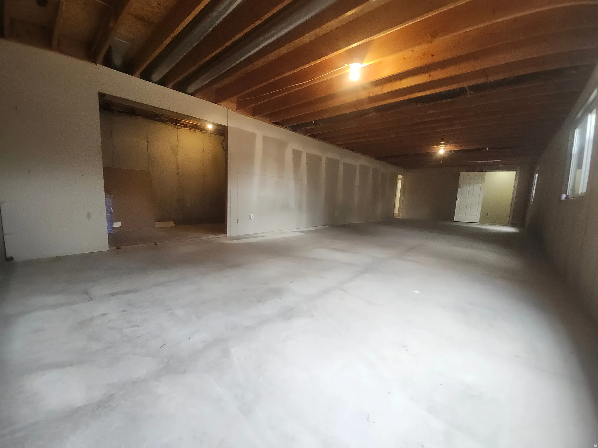 Unfinished Family Room. Spacious open floor plan with polished concrete flooring, exposed wood-beam ceiling with recessed lighting, and multiple room divisions marked by partial walls
