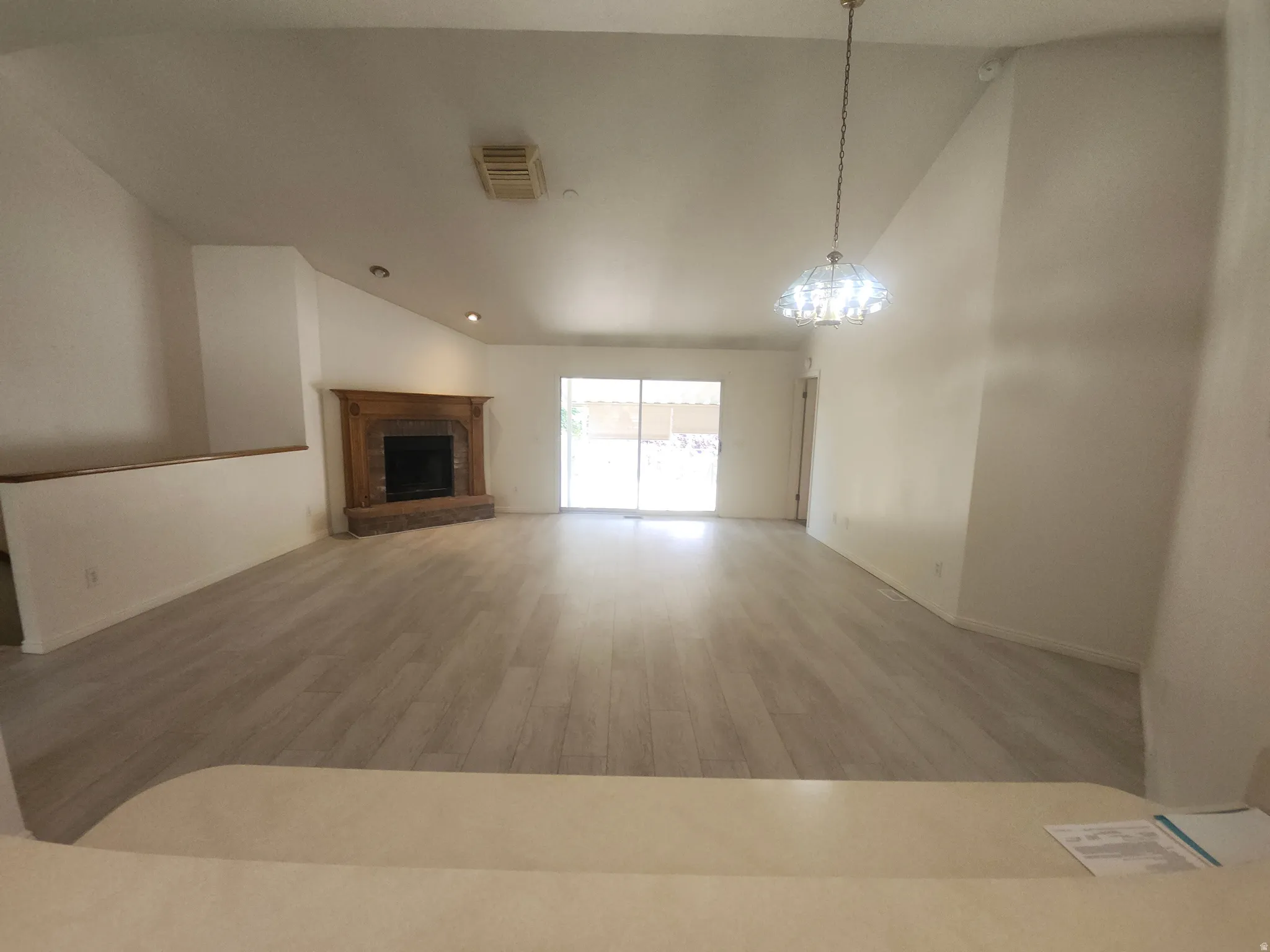 Spacious living area featuring vaulted ceilings, wood-finish flooring, a fireplace with a wood mantle, and sliding glass doors