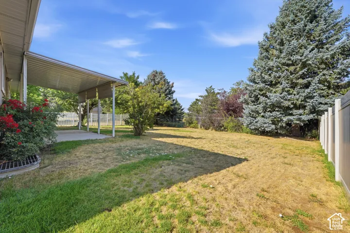 Backyard featuring a covered metal patio, concrete slab, mature trees, and vinyl privacy fencing