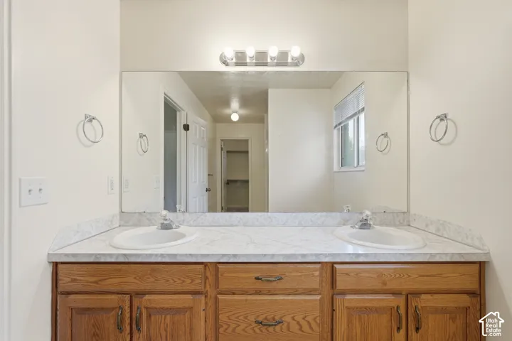 Double vanity featuring a stone-patterned laminate countertop, dual drop-in basins, wood cabinetry, and a large-format mirror with a four-bulb integrated light fixture