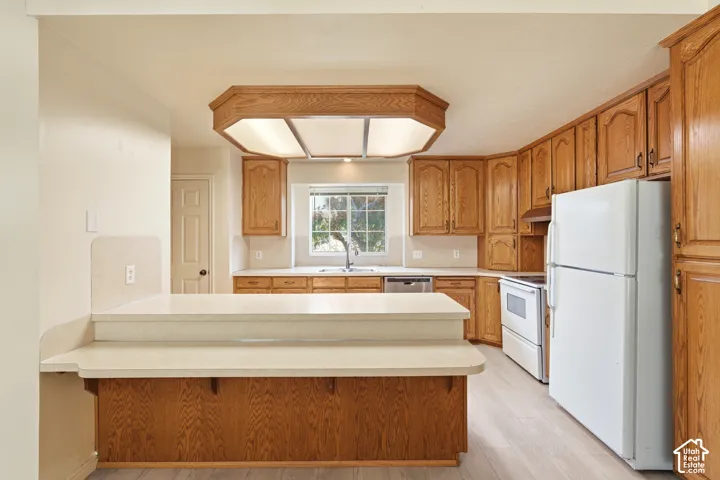 Kitchen featuring wood cabinetry, solid surface countertops, two-tiered breakfast bar, recessed lighting, and wood-finish flooring