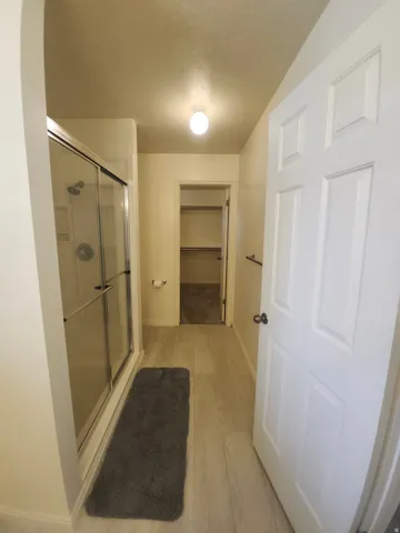 Primary Bedroom Shower, goes to walk-in shower with sliding glass enclosure, light wood-finish flooring, and a paneled interior door
