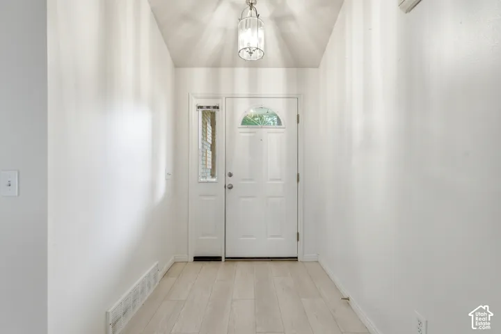 Entryway featuring vaulted ceilings, wood-finish flooring, a pendant light fixture, and an exterior door with a sidelight
