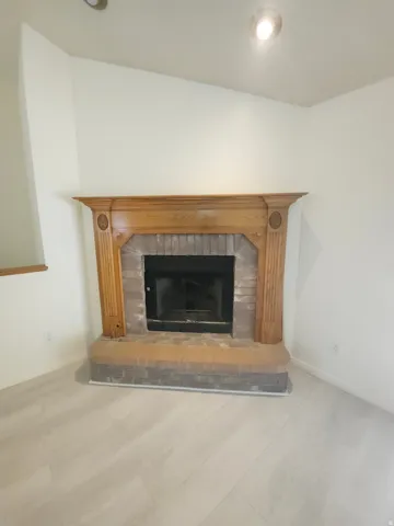 Fireplace with a wood-finish mantel and brick surround, complemented by wood-finish flooring