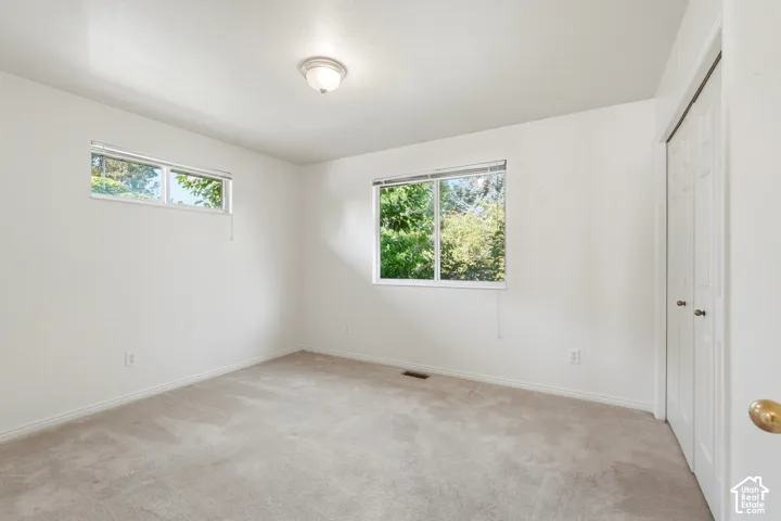 3rd Bedroom/ Neutral interior room featuring neutral-tone carpeting, dual white-framed windows, and double-door closet cabinetry