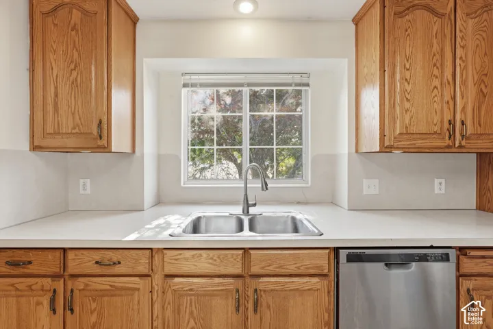 Kitchen featuring wood cabinetry, stainless steel dishwasher, double-basin sink with arched faucet, and solid-surface countertop